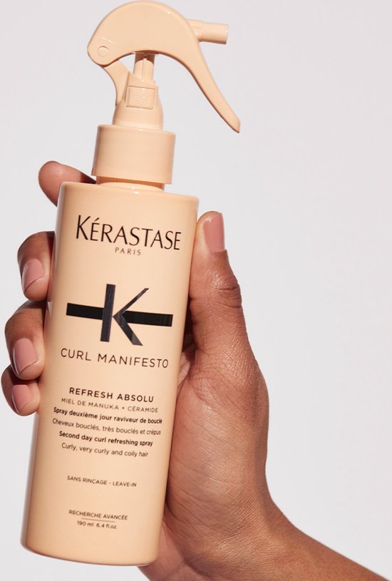 Une main tient le flacon de spray Kérastase Curl Manifesto Refresh Absolu sur fond clair.