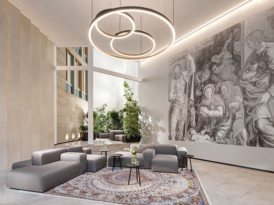 Een moderne lobby met modulaire grijze banken, een groot tapijt met een klassiek patroon en een muurschildering.