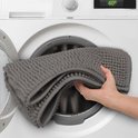 Grijze badmat met bobbelstructuur wordt in een wasmachine gelegd.