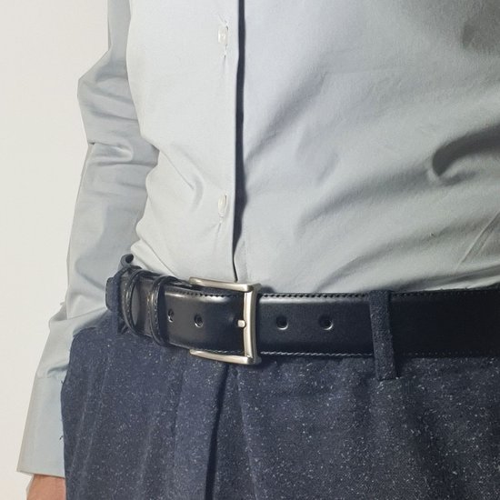 Zwarte leren riem met zilverkleurige gesp, gedragen bij een grijs overhemd en donkerblauwe broek.