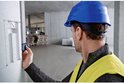Man met blauwe helm en geel hesje gebruikt Bosch laser afstandmeter op een betonnen muur. Groene laserstraal.