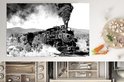 Een zwart-wit afbeelding van een stoomlocomotief die rook en stoom uitstoot tijdens het rijden door een bosrijk gebied.