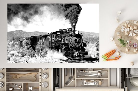 Een zwart-wit afbeelding van een stoomlocomotief die rook en stoom uitstoot tijdens het rijden door een bosrijk gebied.