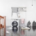 Een wasserette vol water, met een wasmachine, droogrek en wasmand.
