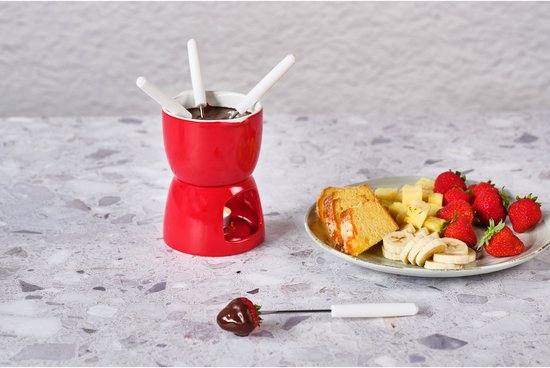 Rode chocolade fondue set met gesneden cake, kaas, aardbeien en een aardbei gedipt in chocolade.