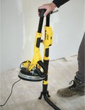 Gele telescoop schuurmachine met schuurkop op de grond. Een persoon met grijze handschoenen houdt de steel vast.