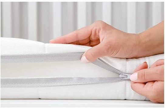 Handen openen een ritssluiting op een witte, gestikte topmatras.