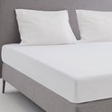 Wit molton hoeslaken op een bed met grijze hoofdbord en kussens.