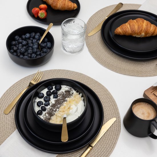Zwarte borden met ontbijt: yoghurt met bosbessen en ontbijtgranen, croisant, aardbeien.