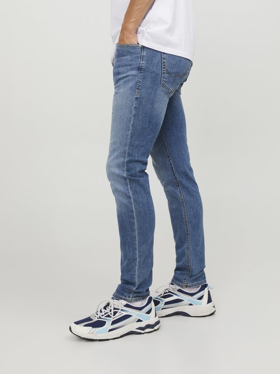 Man in een lichtblauwe skinny jeans en witte sneakers met blauwe accenten.