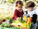Twee jonge kinderen spelen met een John Deere boerderij speeltafel met tractoren en dieren.