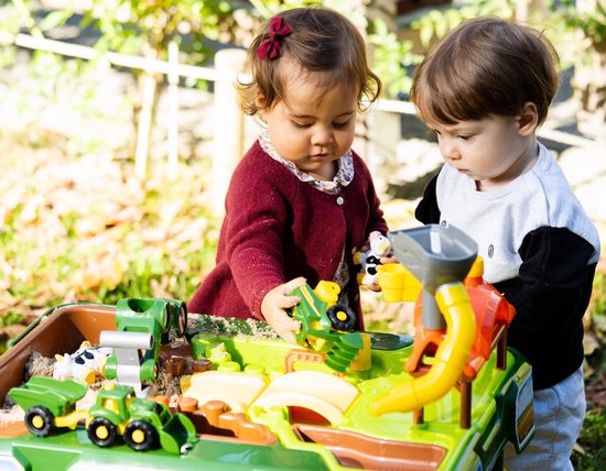Twee jonge kinderen spelen met een John Deere boerderij speeltafel met tractoren en dieren.