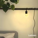 Zwarte fitting met amberkleurige bolvormige lamp, hangend aan een rail boven een bed.