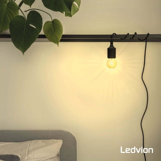 Zwarte fitting met amberkleurige bolvormige lamp, hangend aan een rail boven een bed.