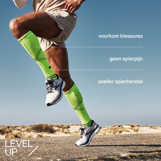 Man met neon-groene compressiesokken die rent op het strand. 'Voorkom blessures', 'geen spierpijn', 'sneller spierherstel'.
