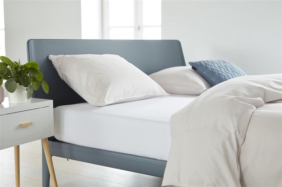 Een wit laken op een grijs bed, met kussens en dekbed.