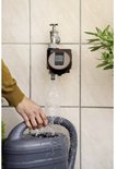Gardena digitale timer met scherm, aangesloten op een waterkraan. Vult een grijze gieter met water.