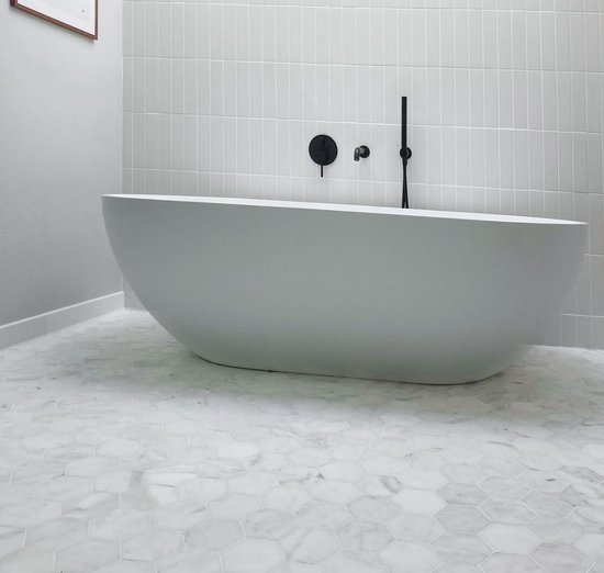 Vrijstaand bad met marmeren hexagon vloer en witte wandtegels.