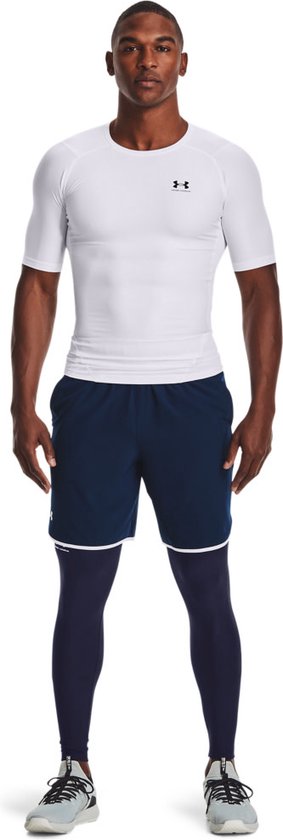 Model draagt wit strak sportshirt, marineblauwe short en blauwe sportlegging van Under Armour.