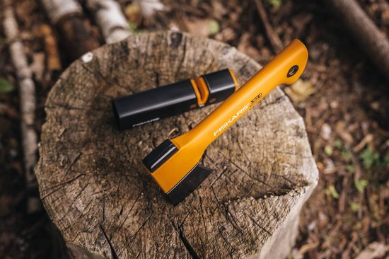 Oranje Fiskars X5E bijl en een zwarte messenslijper op een houten stronk.