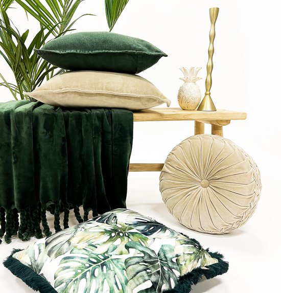 Stapel groene en zandkleurige kussens met donkergroene plaid met franjes.