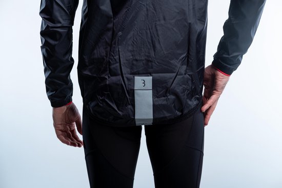 Model toont de achterkant van een zwart fietsjack met reflecterende patch.