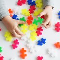 Kinderhanden spelen met veelkleurige Plus-Plus bouwstenen in geel, roze, blauw, groen, oranje en wit.