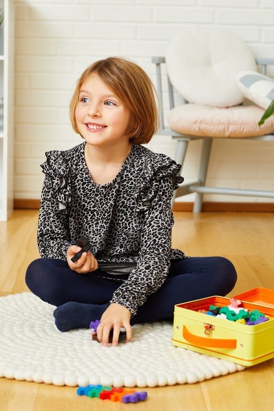 Een meisje met blond haar, in een panterprint shirt, zit op een rond kleed met Plus-Plus bouwstenen.