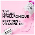 Doorzichtige serum druppelt uit een pipet op een roze achtergrond. Bevat 1,5% hyaluronzuur, peptiden en vitamine B5.