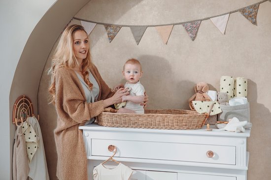 Vrouw met baby in rieten mand op commode. Slingers aan de muur.