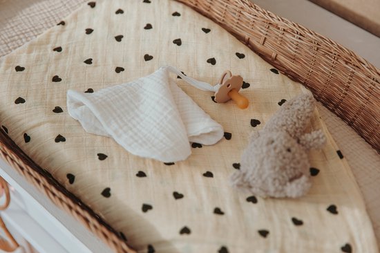 Witte mousseline doek met zwarte hartjesprint, in een rieten mandje. Een speentje en een grijze teddybeer liggen ernaast.