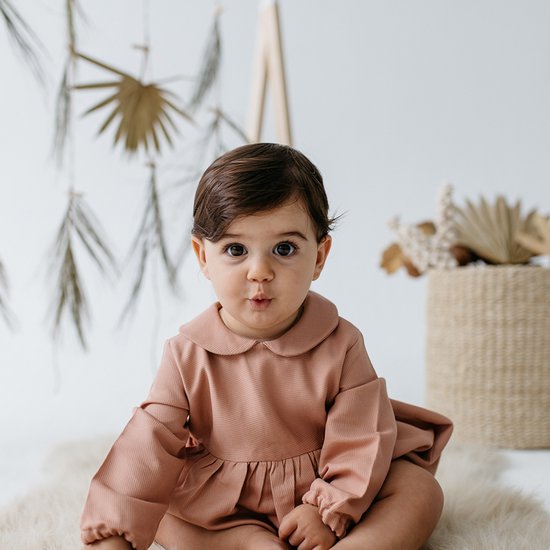 Baby in een oudroze corduroy jumpsuit met peter pan kraag en pofmouwen.