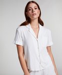 Model met rode haardos, in een wit pyjamashirt met korte mouwen en kraag, gezien vanaf de zijkant.