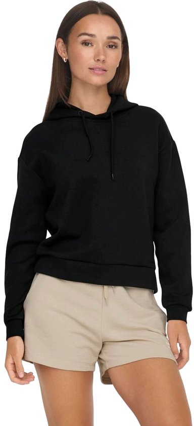 Model draagt een zwarte cropped hoodie en beige shorts.