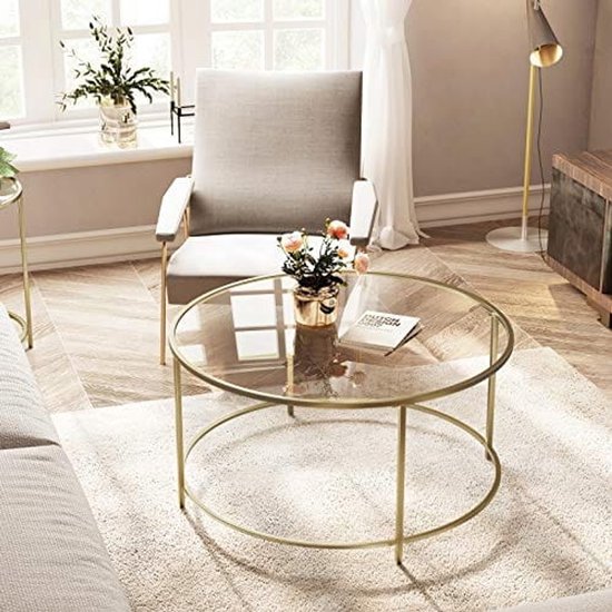 Gouden salontafel met glazen blad, bloemen en boek in een woonkamer.