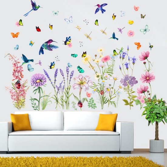 Décoration murale avec des fleurs, des papillons et des colibris au-dessus d'un canapé blanc avec des coussins jaunes.