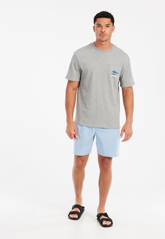 Model in een grijze t-shirt met blauwe golfontwerp op de borstzak en lichtblauwe zwemshort.