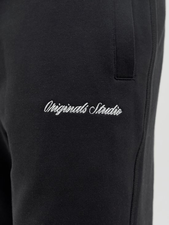 Detail van een zwarte joggingbroek met de geborduurde tekst 'Originals Studio'.