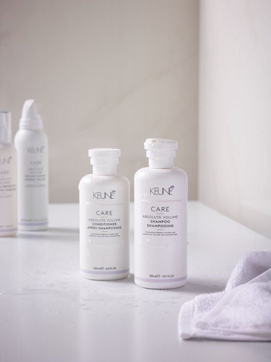 Witte flessen Keune Care Absolute Volume Conditioner (250ml) en shampoo (300ml) in een badkameromgeving met waterdruppels.