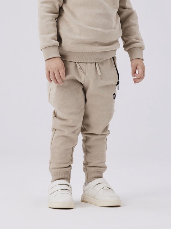Onderkant van een beige joggingbroek met witte sneakers.