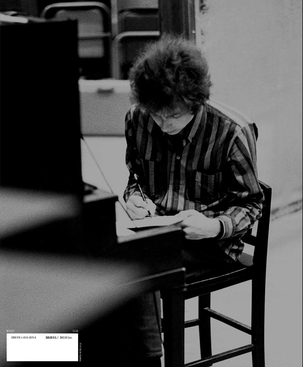 Jonge man met krullend haar, gekleed in een gestreept shirt, schrijft in een boek.