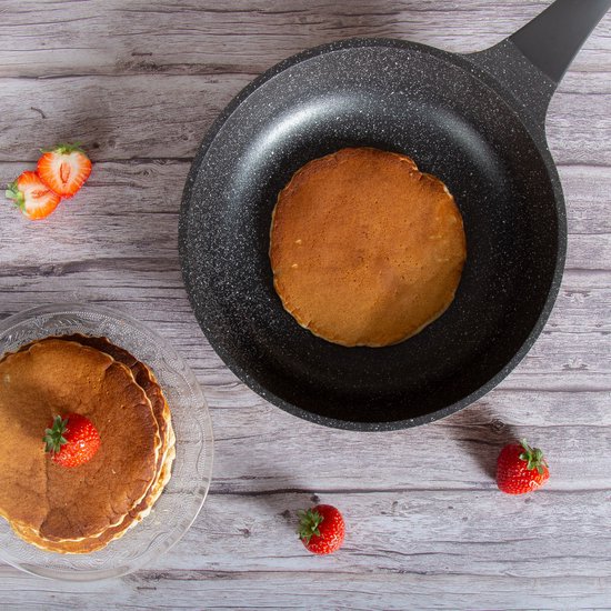 Zwarte koekenpan met een stapel pannenkoeken en aardbeien.