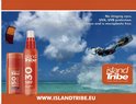 Oranje zonnebrandstick en spray van Island Tribe SPF 50, met een man die kitesurft op de achtergrond.