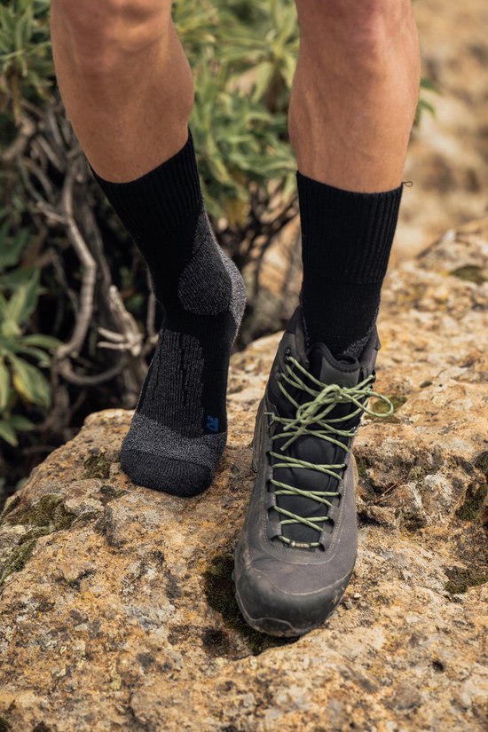 Voeten van een man in zwarte wandelsokken met grijze accenten, naast een grijze wandelschoen.