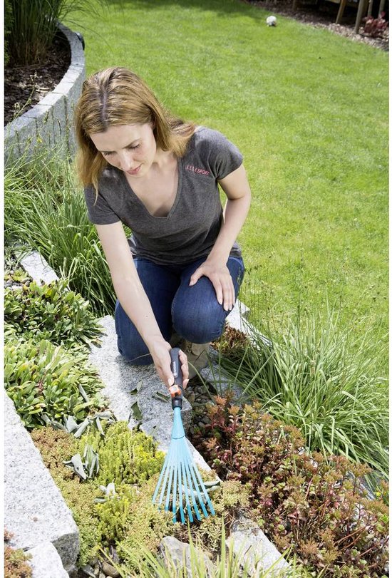 Vrouw met grijs shirt gebruikt een turquoise Gardena-waaierhark om planten in een rotstuin te verzorgen.