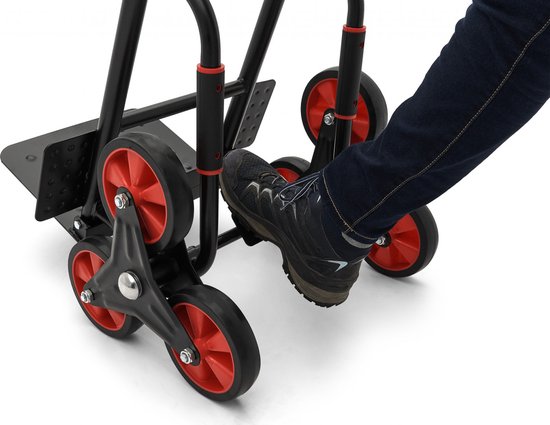 Voet op de pedalen van de zwarte steekwagen met rode wielstellen.