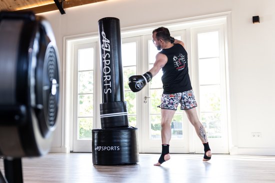 Man traint met AJ-Sports bokszak van 175cm, draagt zwart shirt en korte broek met print.