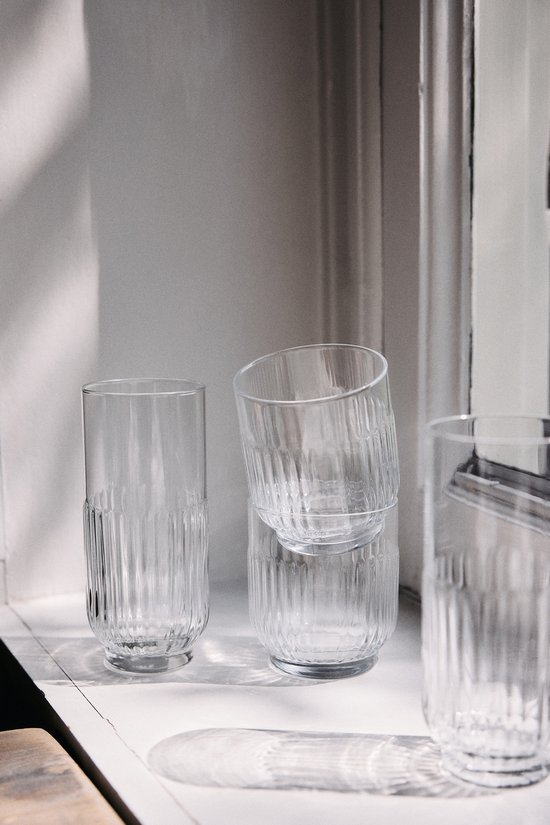 Trois verres transparents à côtes verticales, sur un rebord de fenêtre.