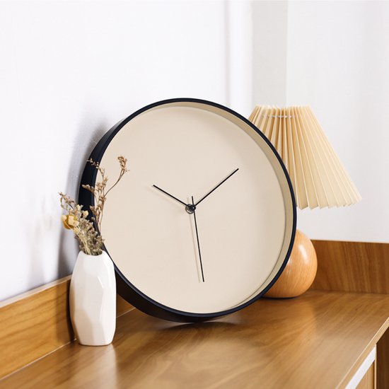 Horloge ronde beige avec bordure noire, posée sur une table en bois avec décoration.