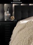 Zwarte tafellamp met grote gloeilamp op een nachtkastje naast een bed met beige sprei.